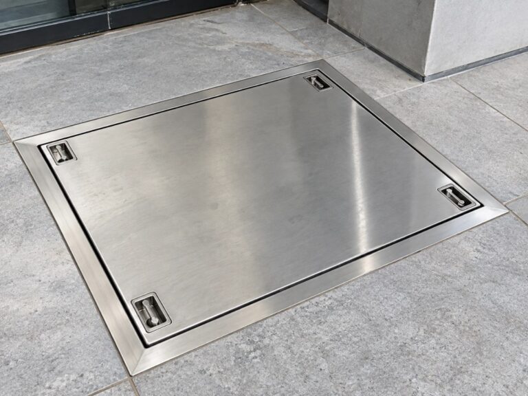 Stainless steel manhole cover and frame with lifting keys, installed in a tiled floor